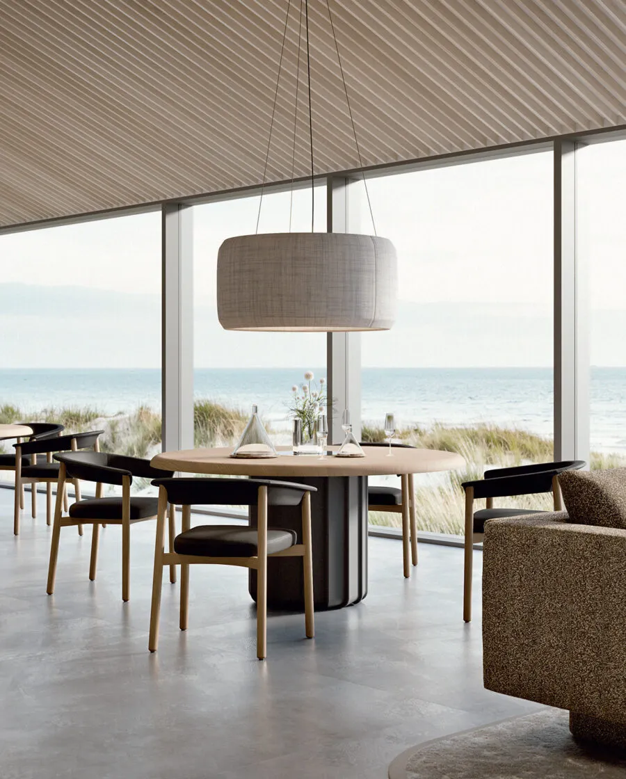 Lash wooden chair design in natural oak with black seat around an oval black table in a coastal space with sea and dunes view — Sabree Italian design