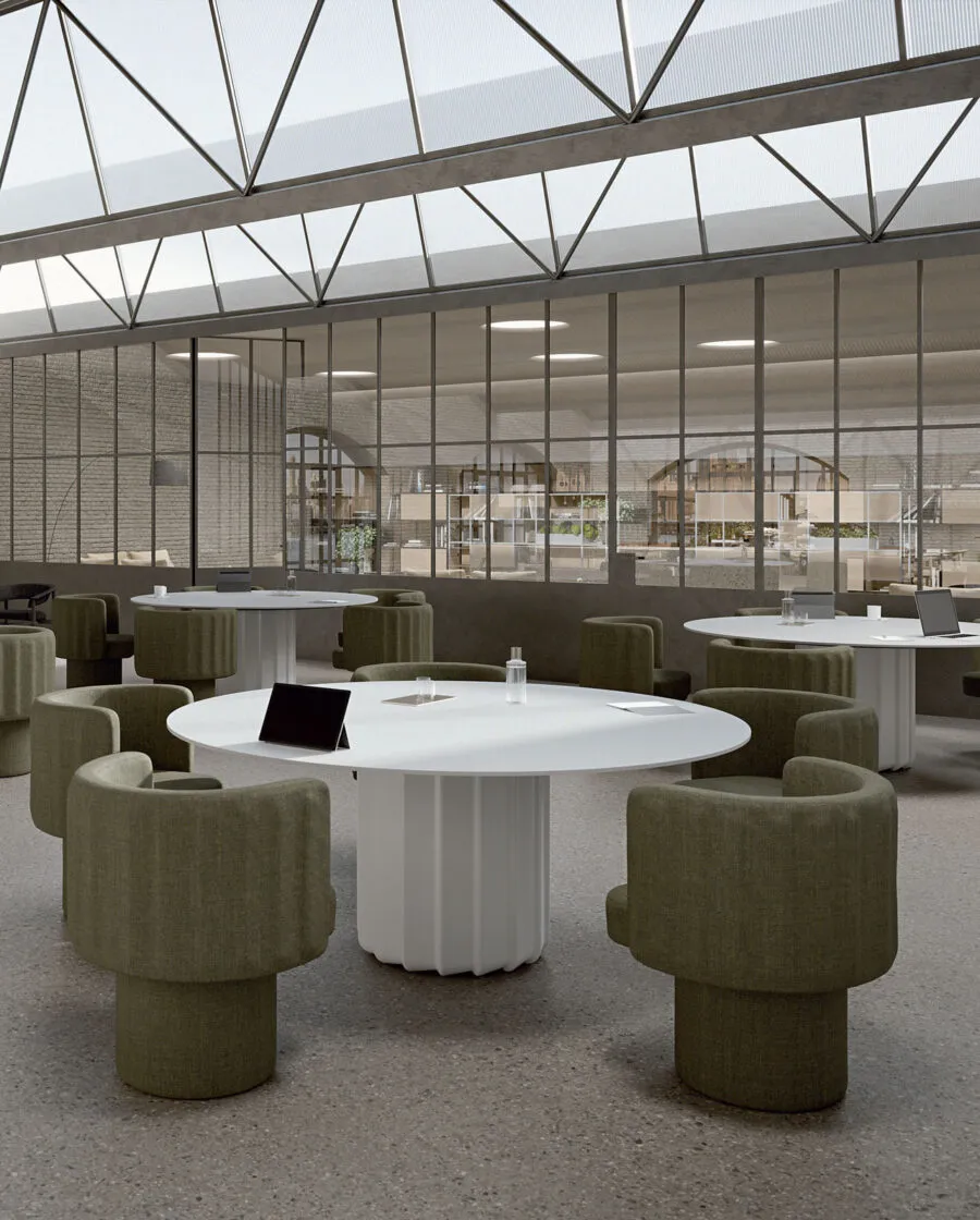 Sabree tub chairs in green upholstery around a white round table in a contemporary collaborative workspace with industrial glass roof and terrazzo floor — Italian design