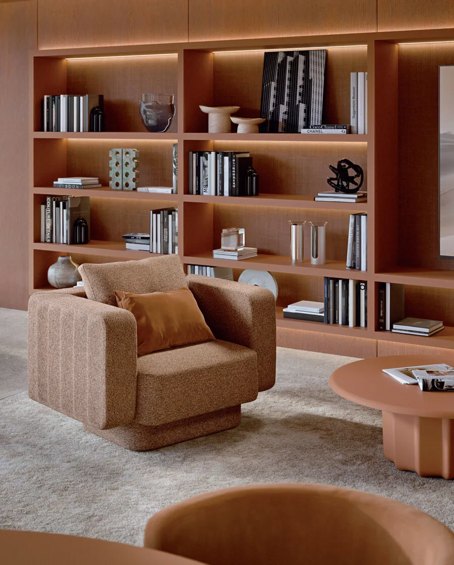 Sabree designer armchair in camel upholstery in a warm private library with oak shelving and terracotta tones — Italian design