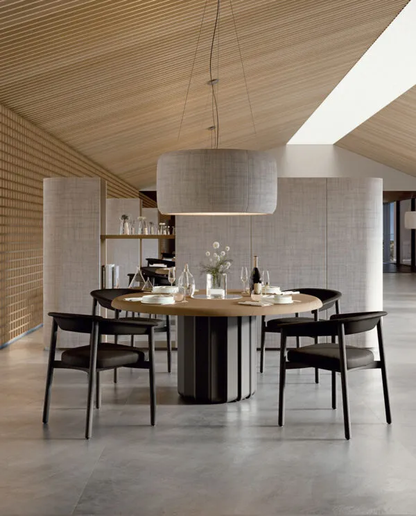 Sabree round table design with dark sculptural base and oak top, surrounded by Lash chairs in a resort restaurant with wooden ceiling and natural light — Frezza contract